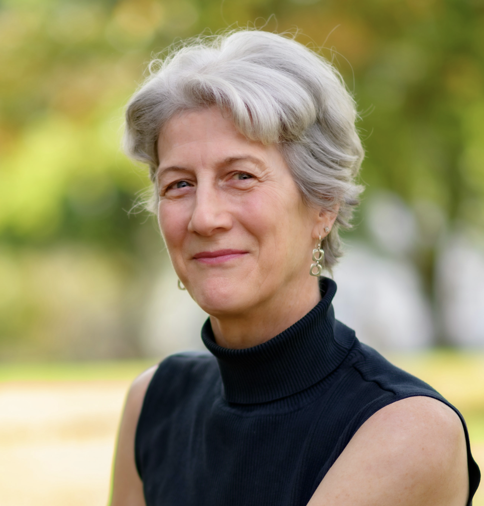 Headshot of Caucasian author, smiling with head tilted. Gray hair, blue eyes, black turtleneck.