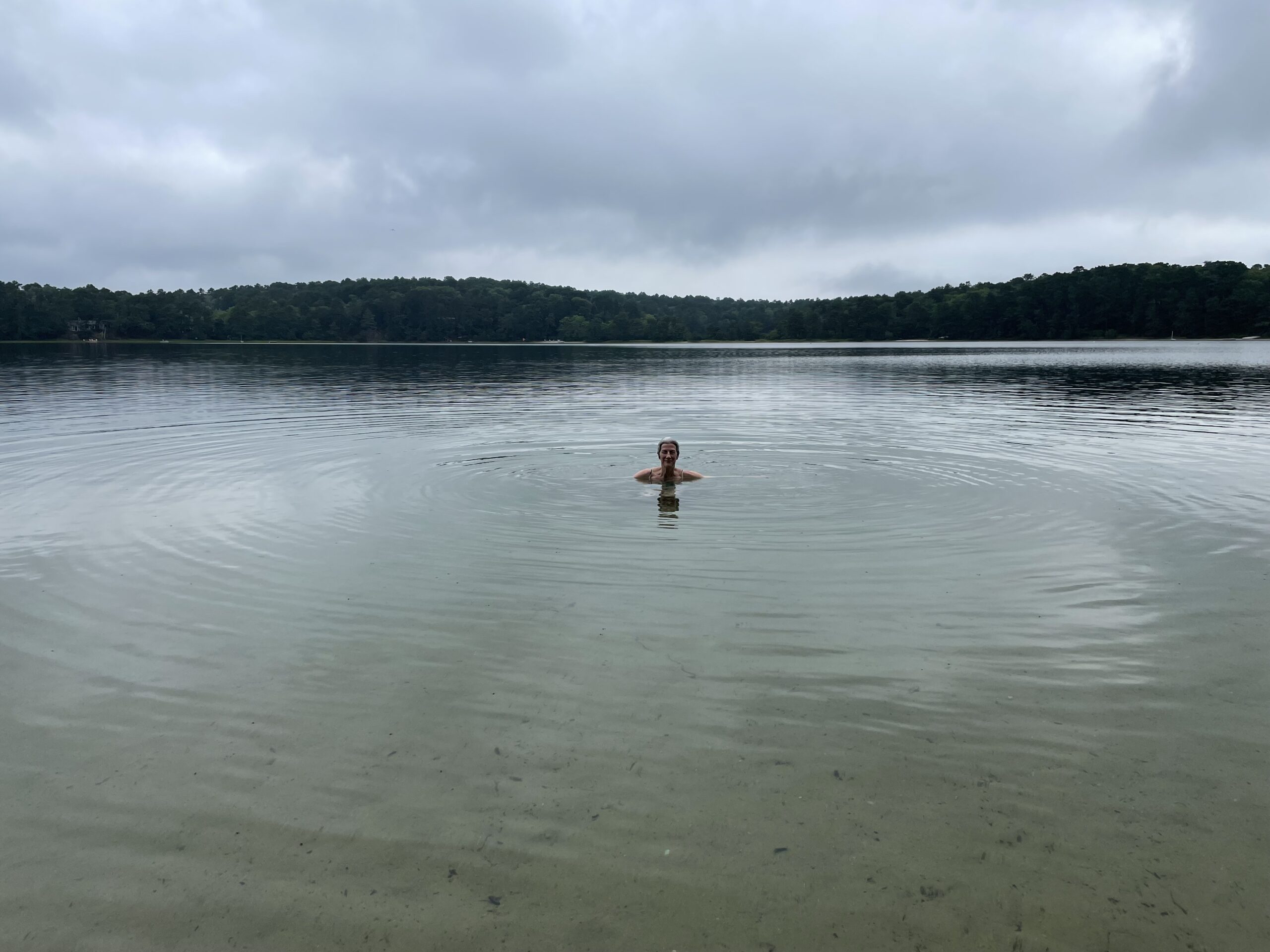 Photo of author in Great Pond, Wellfleet, Massachusetts. Author is submerged up to her shoulders. She is the only person in the pond, which is ringed with trees.